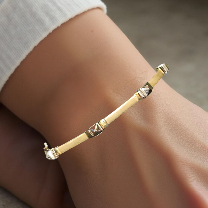 Gold bracelet with geometric designs on a wrist against a neutral background