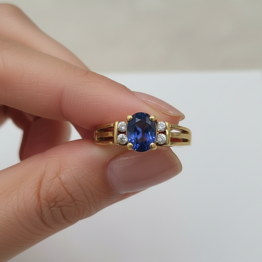 Gold ring with a blue gemstone held by a hand against a neutral background