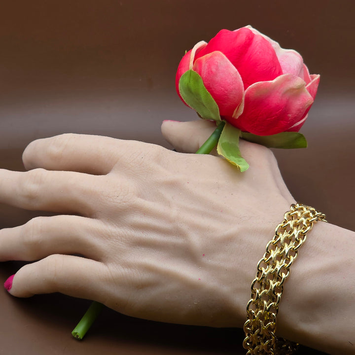 Hand holding a pink flower with a gold chain bracelet on a brown background
