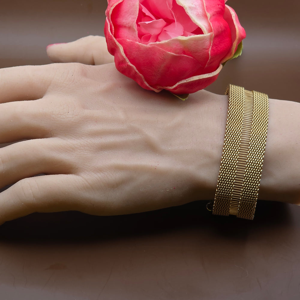 Hand wearing a gold bracelet with a pink flower against a brown background