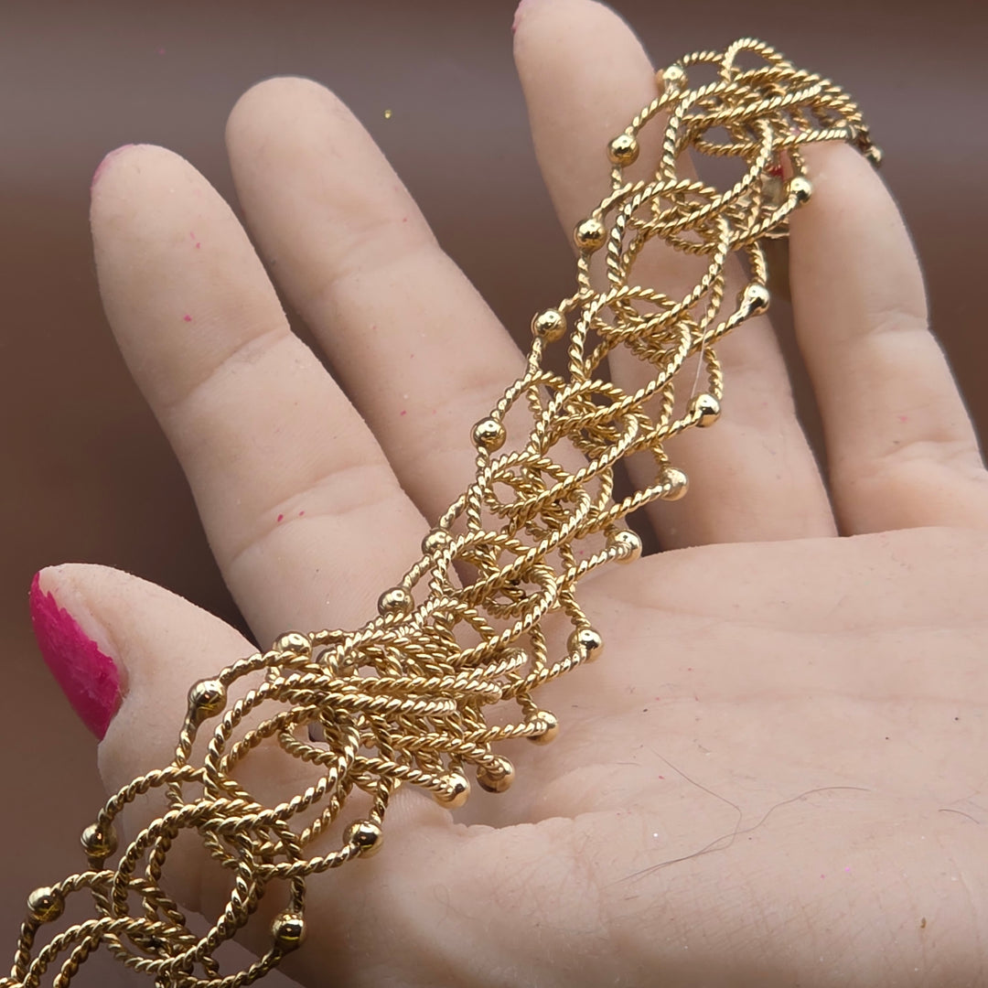 Gold bracelet being held on a hand with a blurred background