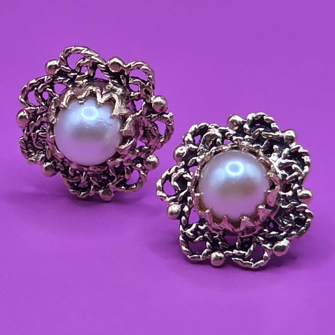 Pair of gold-framed pearl earrings on a purple background