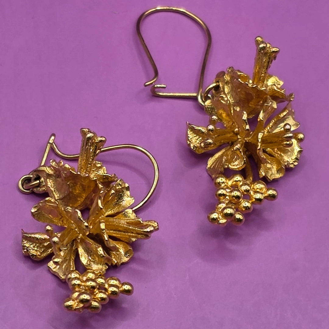 Pair of gold floral earrings on a purple background
