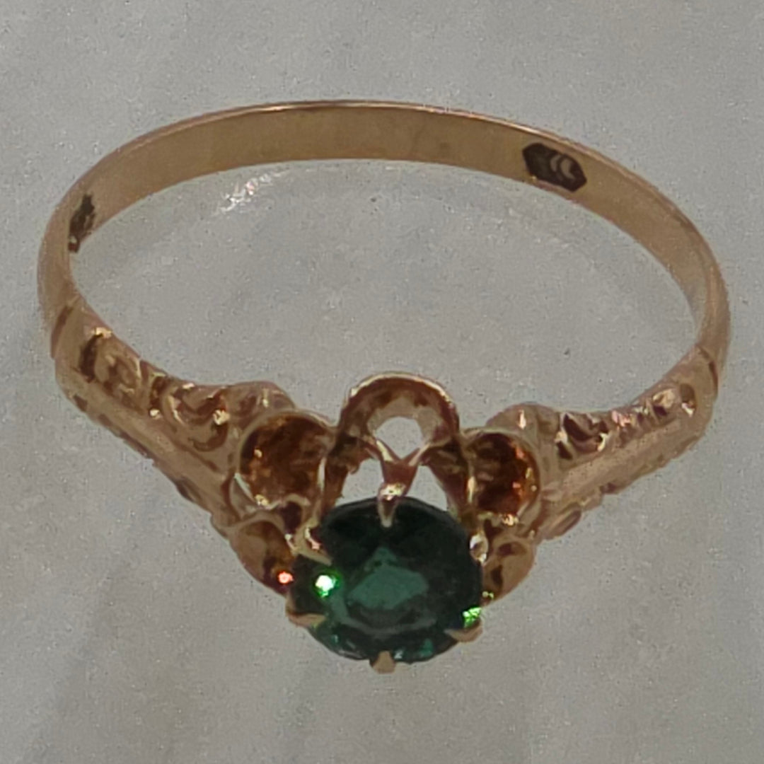 Gold ring with a green gemstone on a light gray background