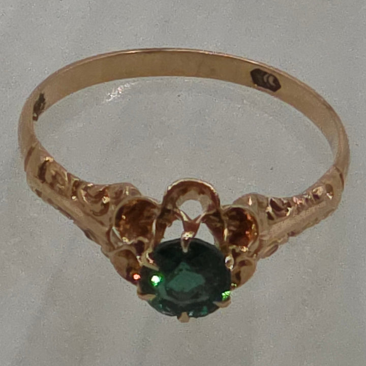 Gold ring with a green gemstone on a light gray background