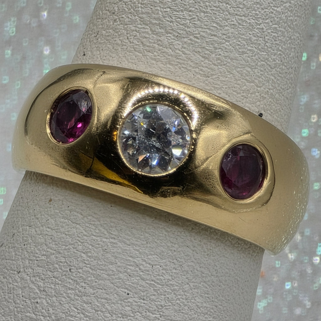 Gold ring with a central diamond and two rubies on a textured surface