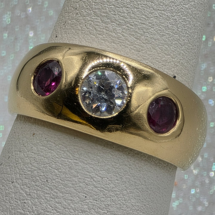 Gold ring with a central diamond and two rubies on a textured surface
