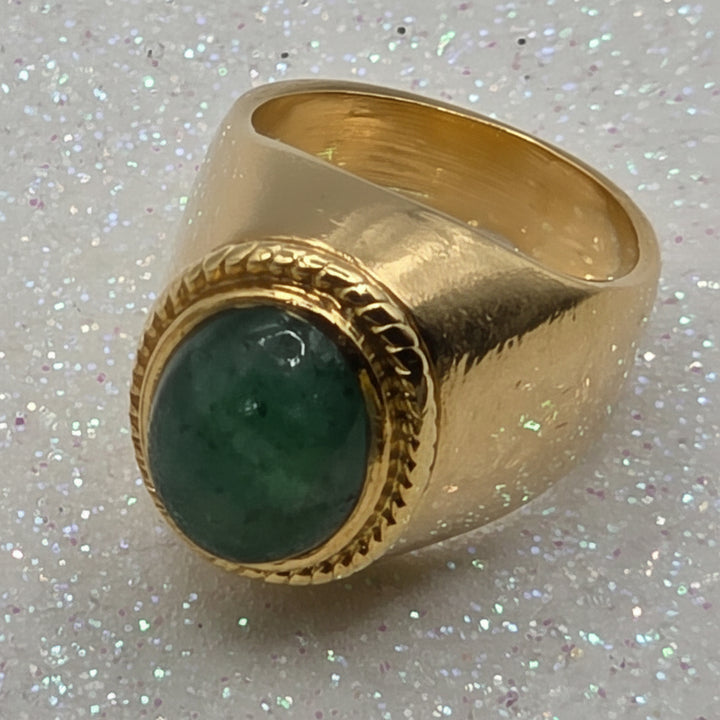 Gold ring with a green jade on a glittery white background