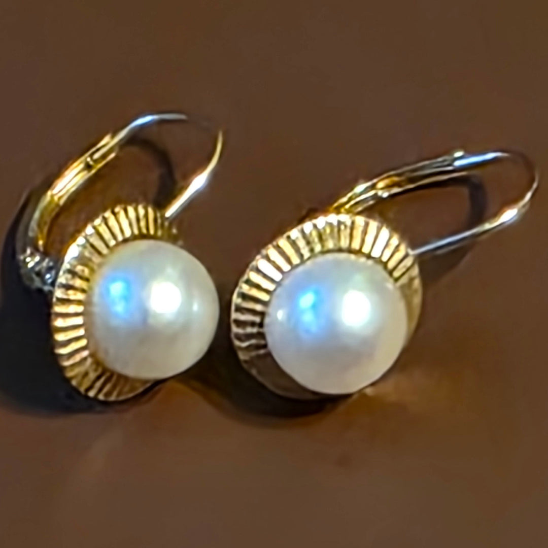 Pair of pearl earrings with gold accents on a reflective surface