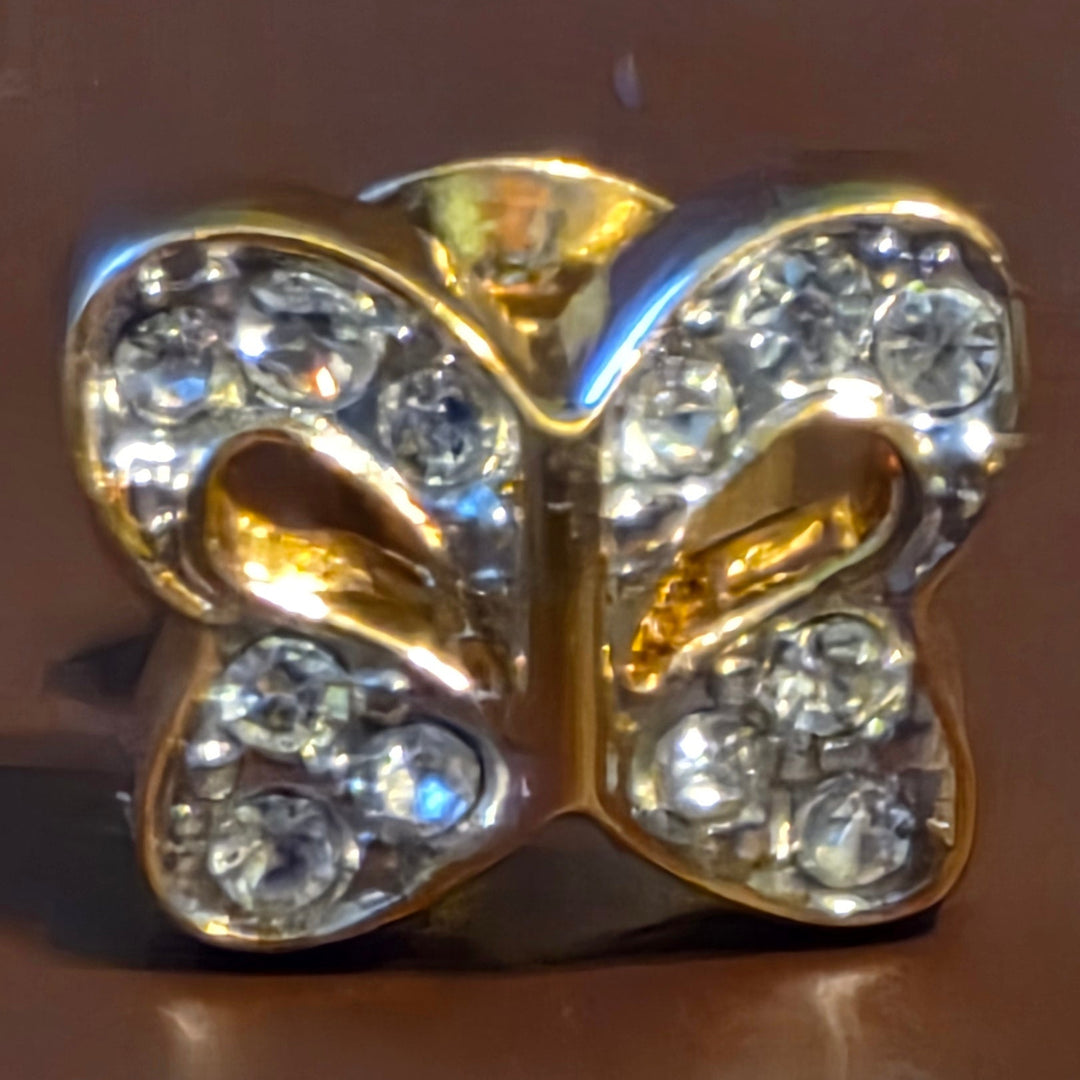 Gold butterfly-shaped jewelry with embedded crystals on a brown background