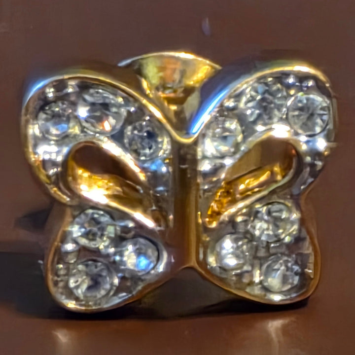 Gold butterfly-shaped jewelry with embedded crystals on a brown background