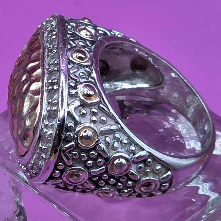 Silver ring with intricate design on a purple surface