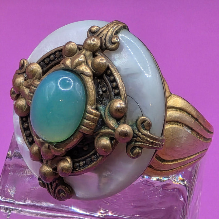 Decorative ring with turquoise stone and gold detailing on a purple background