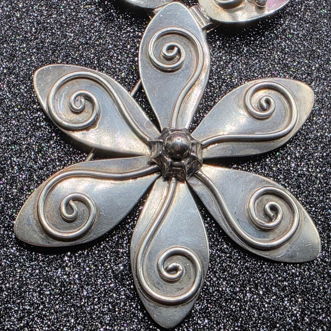 Silver floral brooch with intricate designs on a black textured background