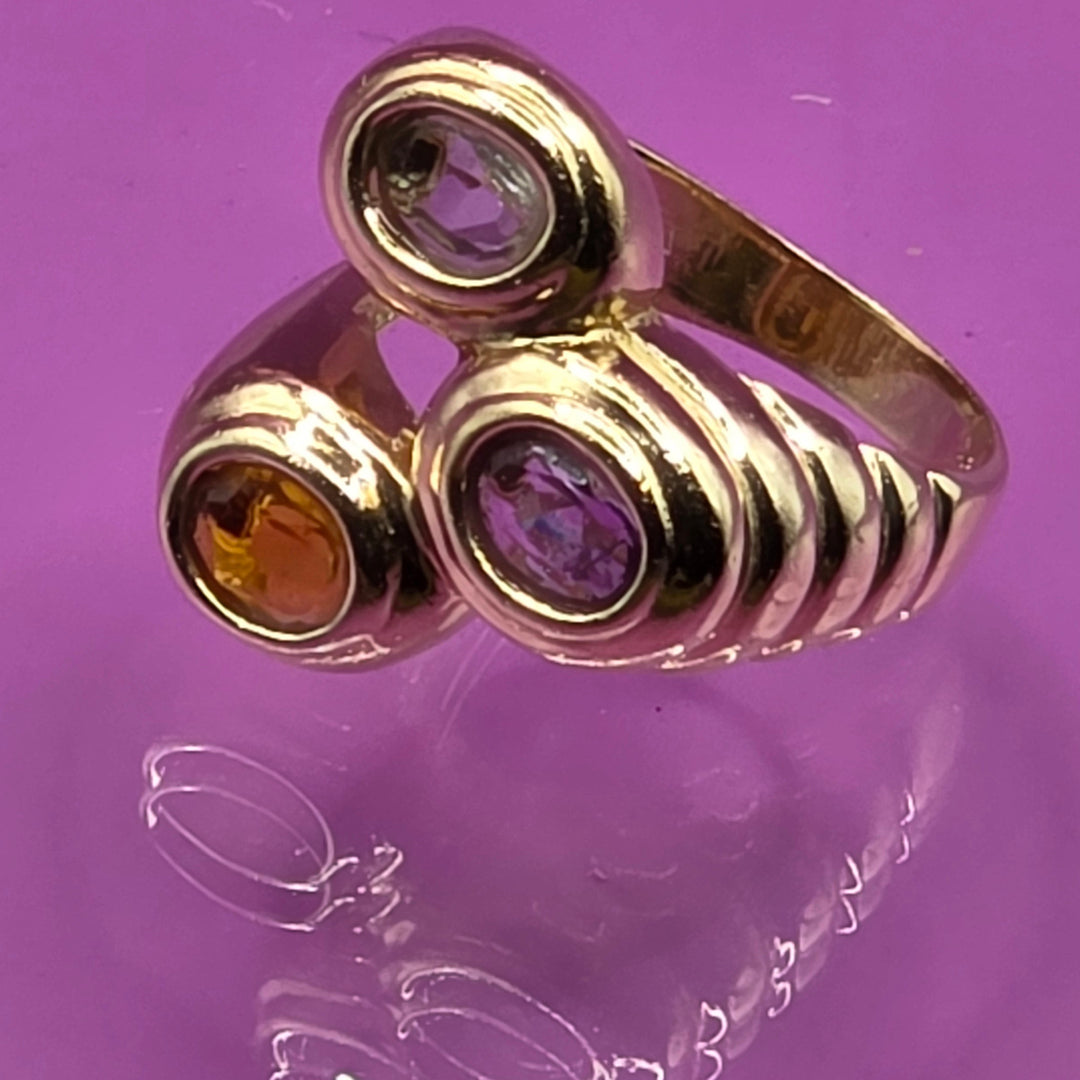 Gold ring with three gemstones on a purple surface